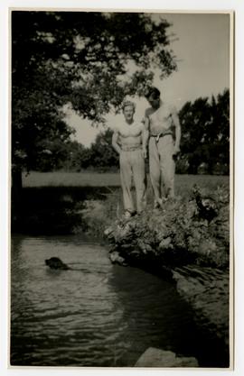 Two men and a dog swimming in a pond