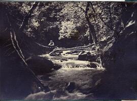Man sitting on log crossing stream