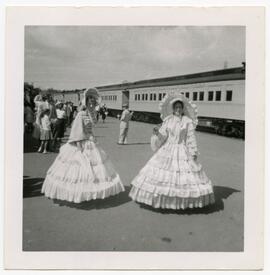Two women wearing large dresses for a parade, standing in front of CNR train