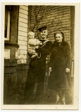 Man in Navy uniform holding a baby and a woman in a fur coat