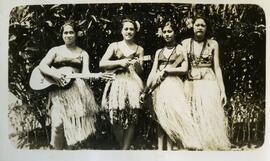 Four women in grass skirts with guitars